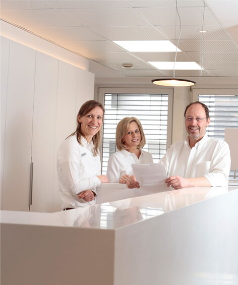 Dr. Hartmut Schröder, Dr. Antje Kühn und Dr. Breddin Böttcher stehen nebeneinander im Eingangsbereich der Praxis.