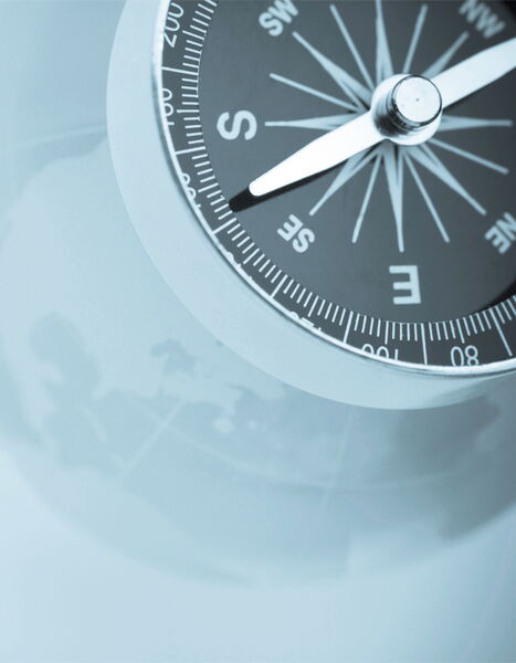 Angeschnittener Kompass, nur teilweise sichtbar, vor grauem Hintergrund.